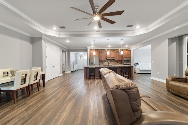 living room featuring a tray ceiling, ceiling fan, ornamental molding, and dark hardwood / wood-style floors