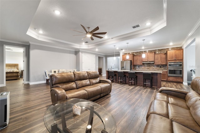 living room with dark hardwood / wood-style flooring, a tray ceiling, ceiling fan, and ornamental molding