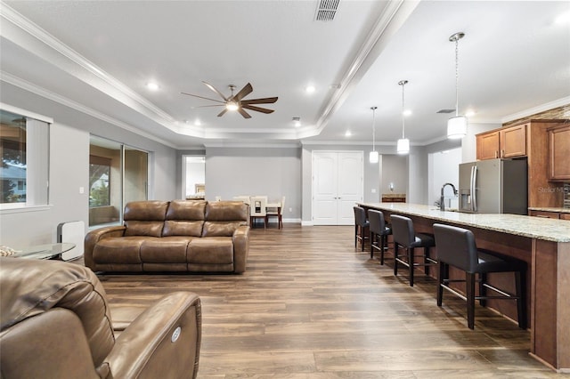 living room featuring dark hardwood / wood-style flooring, ornamental molding, a raised ceiling, ceiling fan, and sink