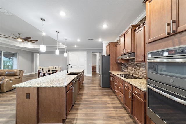 kitchen featuring stainless steel appliances, crown molding, decorative light fixtures, decorative backsplash, and a center island with sink