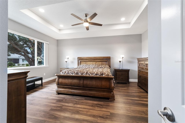 bedroom with ceiling fan, dark wood-type flooring, and a tray ceiling