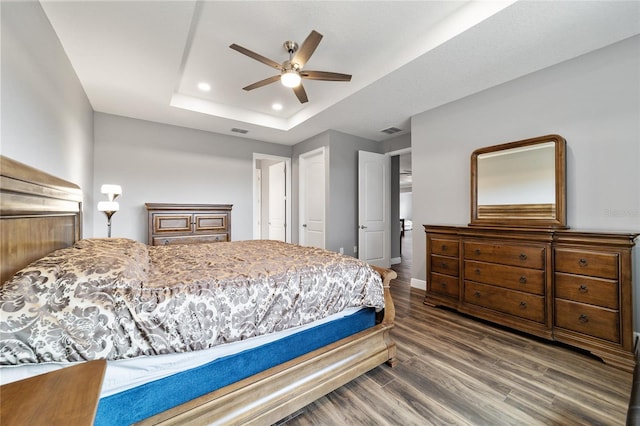 bedroom with ceiling fan, dark hardwood / wood-style flooring, and a tray ceiling