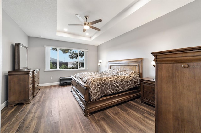 bedroom featuring ceiling fan, a raised ceiling, and dark wood-type flooring