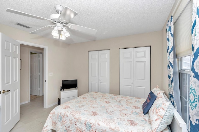 bedroom with ceiling fan, light tile patterned floors, a textured ceiling, and two closets