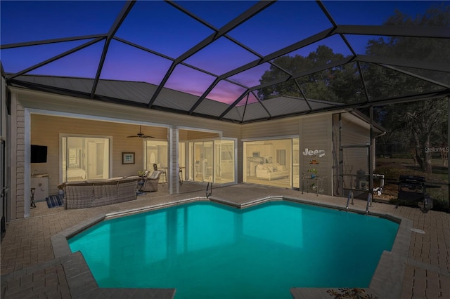 pool at dusk featuring outdoor lounge area, glass enclosure, ceiling fan, and a patio