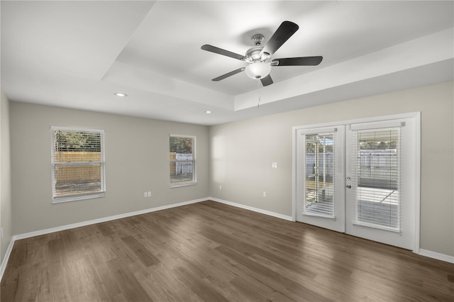 unfurnished room with a tray ceiling, dark hardwood / wood-style flooring, ceiling fan, and french doors