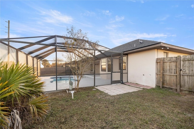 rear view of property featuring a fenced in pool, glass enclosure, a patio area, and a yard