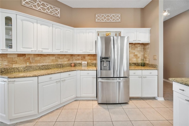 kitchen with light tile patterned floors, white cabinetry, light stone countertops, stainless steel fridge with ice dispenser, and decorative backsplash