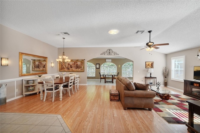 living room featuring lofted ceiling, ceiling fan with notable chandelier, light hardwood / wood-style floors, and a textured ceiling