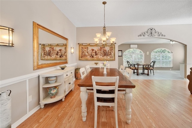 dining area with ceiling fan with notable chandelier, vaulted ceiling, and light hardwood / wood-style floors