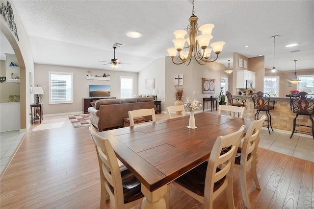 dining area featuring ceiling fan with notable chandelier, light hardwood / wood-style flooring, a textured ceiling, and vaulted ceiling