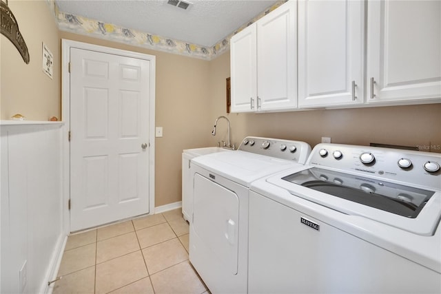 clothes washing area featuring light tile patterned flooring, sink, cabinets, a textured ceiling, and independent washer and dryer