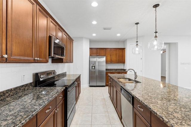 kitchen featuring dark stone counters, sink, light tile patterned floors, appliances with stainless steel finishes, and decorative light fixtures