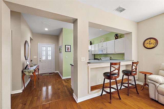 kitchen with dark hardwood / wood-style flooring, kitchen peninsula, white appliances, a kitchen bar, and white cabinets