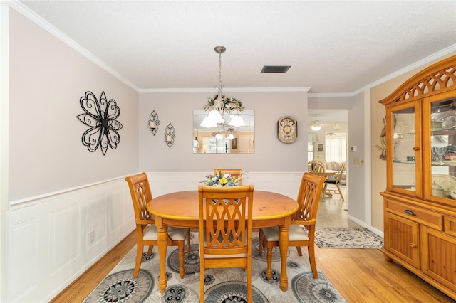 dining space featuring a notable chandelier, crown molding, a textured ceiling, and light hardwood / wood-style flooring