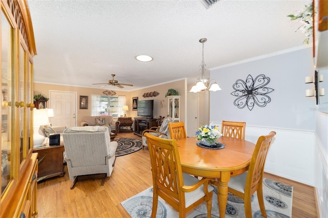 dining area with a textured ceiling, ceiling fan with notable chandelier, light hardwood / wood-style floors, and crown molding