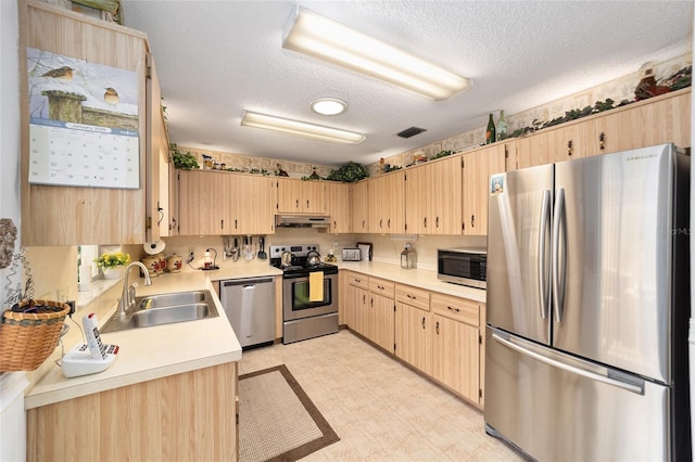 kitchen featuring appliances with stainless steel finishes, a textured ceiling, light brown cabinetry, and sink