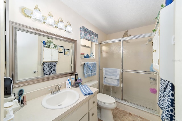 bathroom with a textured ceiling, vanity, toilet, and walk in shower