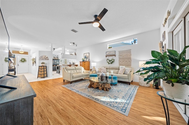 living room featuring ceiling fan, light wood-type flooring, and a textured ceiling