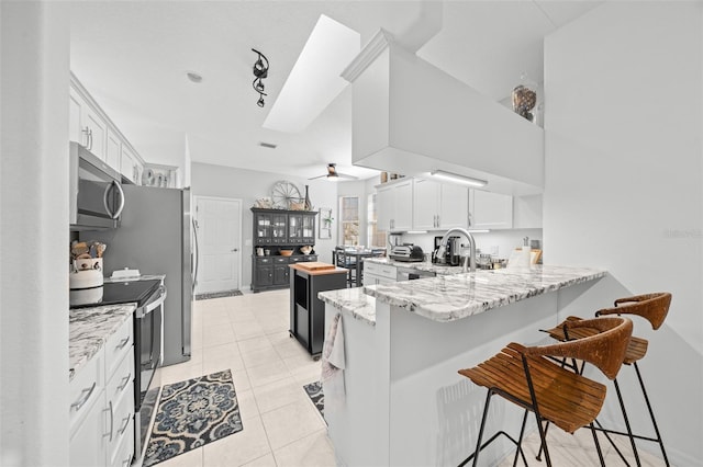 kitchen with a kitchen bar, kitchen peninsula, stainless steel appliances, ceiling fan, and white cabinets