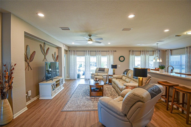 living room with a textured ceiling, light hardwood / wood-style flooring, and ceiling fan