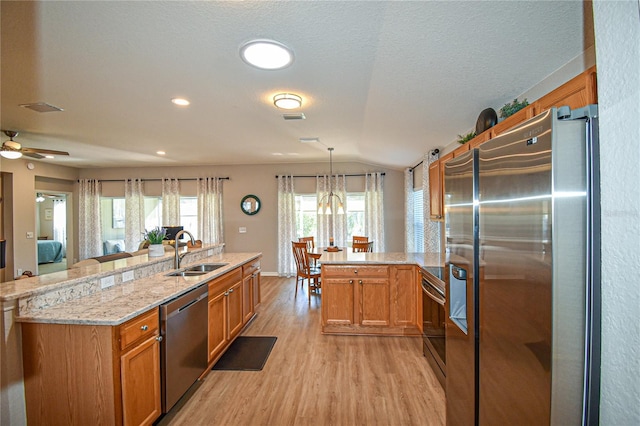 kitchen featuring hanging light fixtures, sink, vaulted ceiling, light wood-type flooring, and appliances with stainless steel finishes