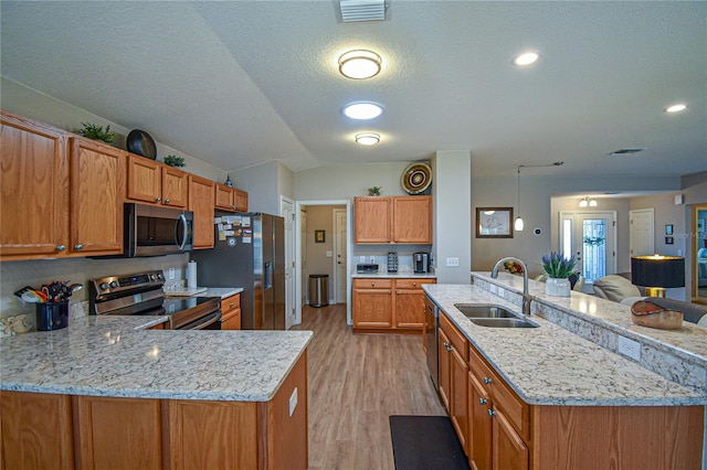 kitchen with light wood-type flooring, a textured ceiling, stainless steel appliances, sink, and lofted ceiling