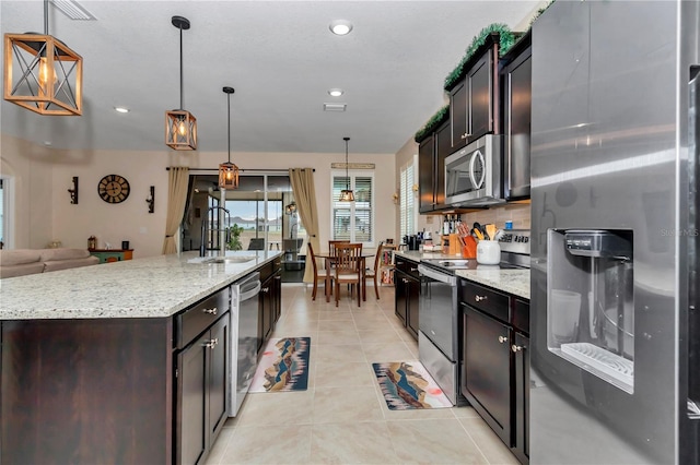 kitchen with a kitchen island with sink, appliances with stainless steel finishes, sink, decorative light fixtures, and light tile patterned flooring