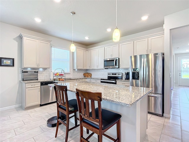 kitchen featuring light stone countertops, a center island, stainless steel appliances, pendant lighting, and light tile patterned floors