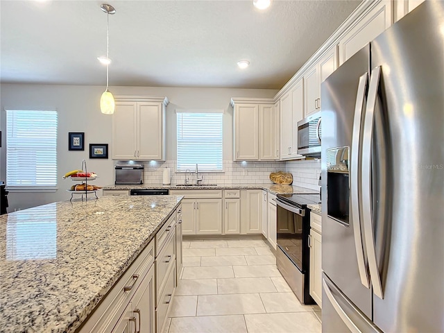 kitchen featuring light stone countertops, appliances with stainless steel finishes, sink, pendant lighting, and white cabinets