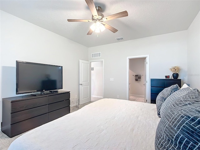 bedroom with ceiling fan, light colored carpet, a textured ceiling, and ensuite bath