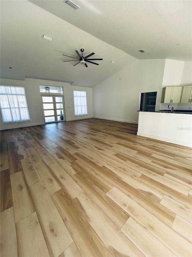 unfurnished living room featuring vaulted ceiling, light hardwood / wood-style floors, french doors, and ceiling fan