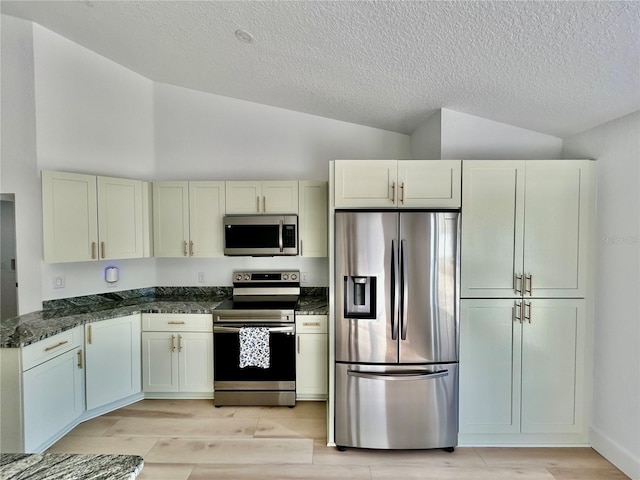 kitchen featuring high vaulted ceiling, appliances with stainless steel finishes, light hardwood / wood-style floors, and dark stone countertops