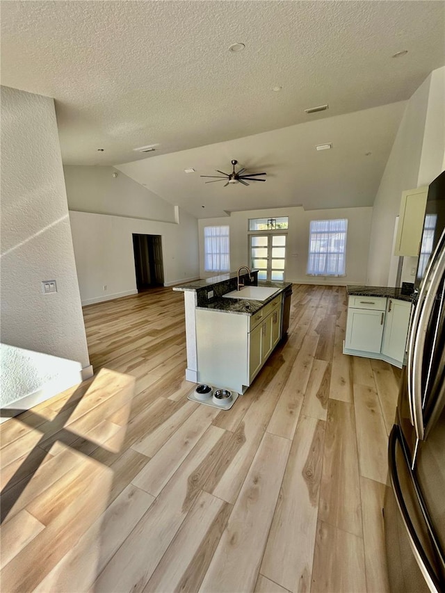 kitchen featuring stainless steel refrigerator, sink, white cabinets, dark stone counters, and a center island with sink