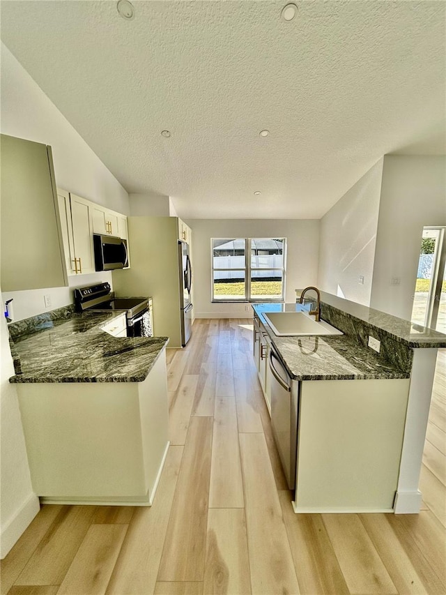 kitchen featuring sink, appliances with stainless steel finishes, light hardwood / wood-style floors, white cabinets, and dark stone counters