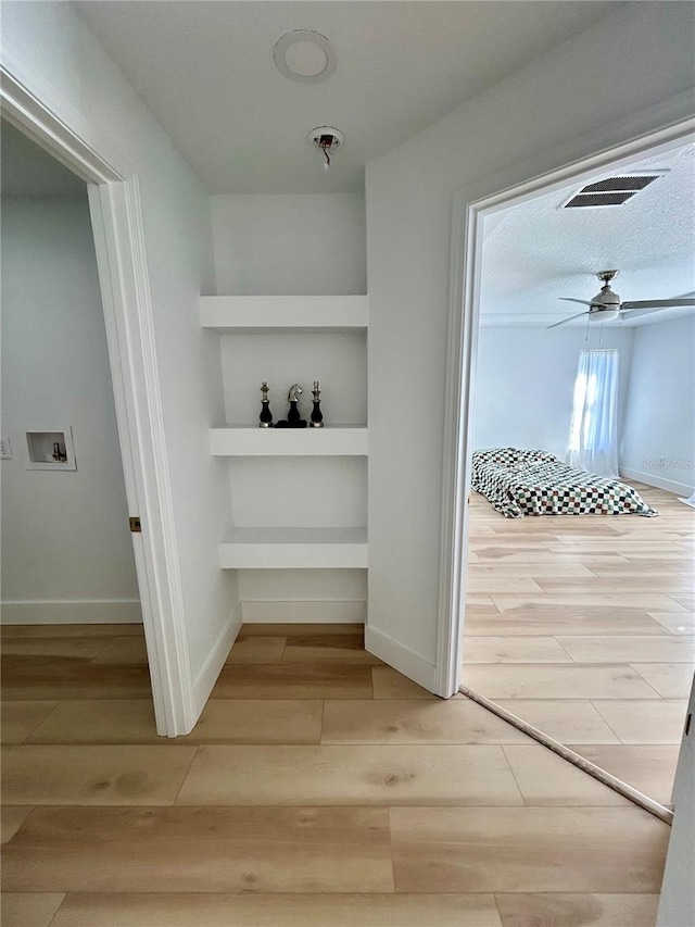 corridor with light hardwood / wood-style floors, built in features, and a textured ceiling