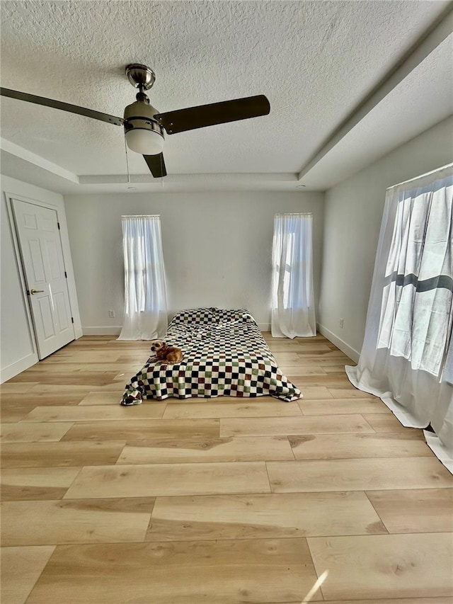 bedroom featuring multiple windows, a tray ceiling, and ceiling fan