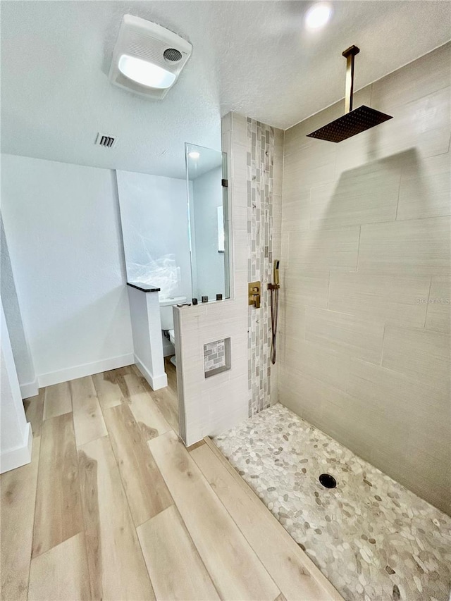 bathroom featuring wood-type flooring, tiled shower, and a textured ceiling