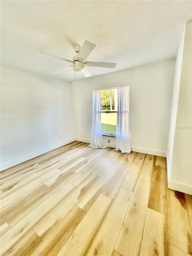 empty room with a textured ceiling, ceiling fan, and light hardwood / wood-style flooring