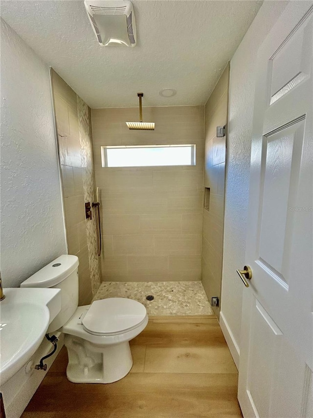 bathroom with toilet, sink, a textured ceiling, a tile shower, and hardwood / wood-style floors