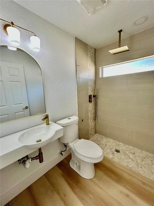 bathroom featuring tiled shower, toilet, sink, a textured ceiling, and hardwood / wood-style floors