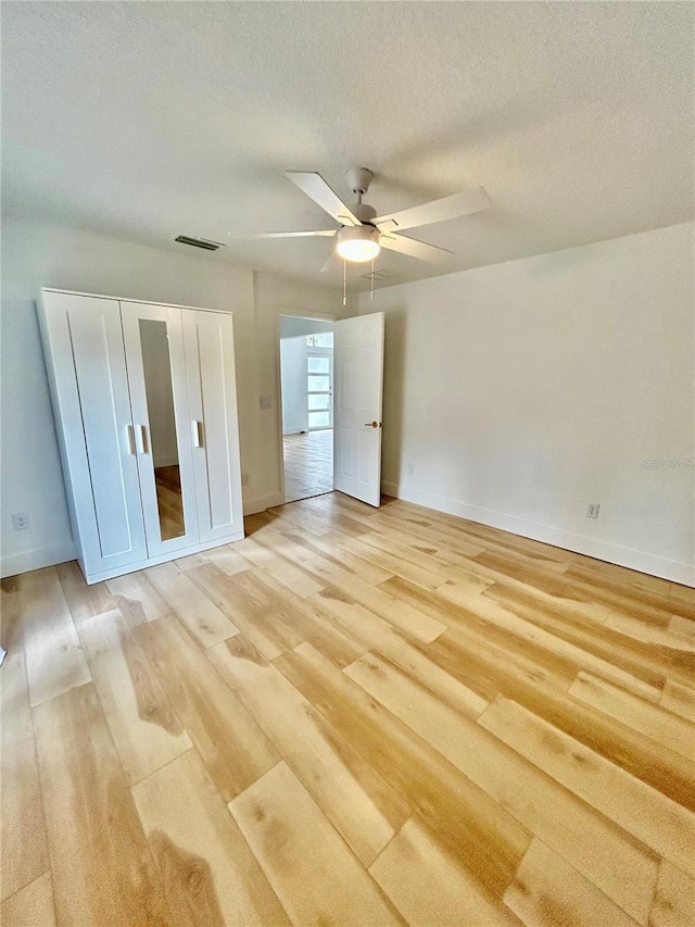 unfurnished bedroom with ceiling fan, light hardwood / wood-style floors, a closet, and a textured ceiling