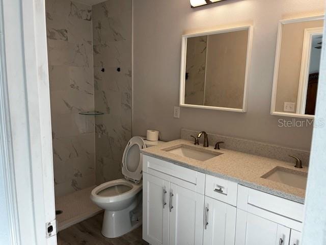 bathroom with double vanity, toilet, a tile shower, and a sink