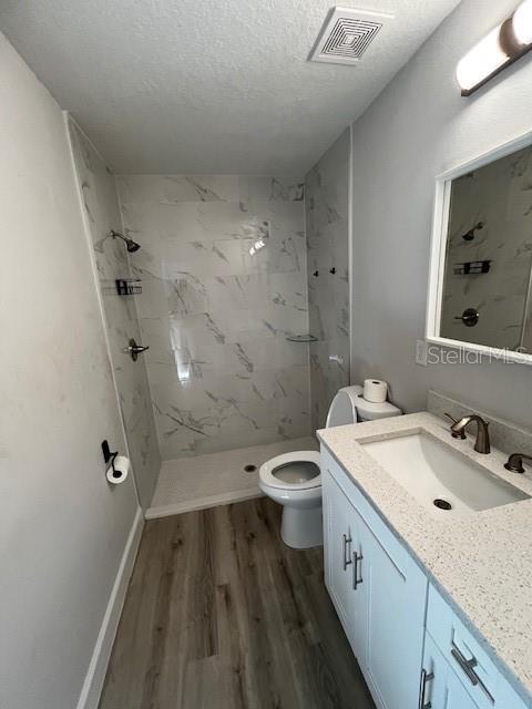 bathroom featuring a marble finish shower, visible vents, wood finished floors, and vanity