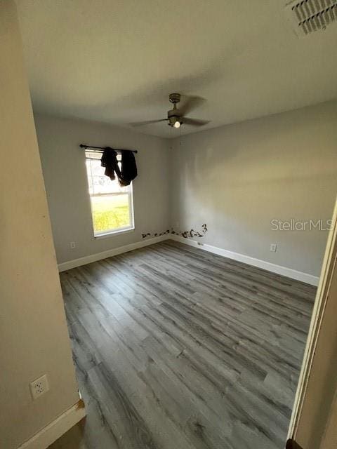 empty room featuring dark wood-type flooring, visible vents, ceiling fan, and baseboards