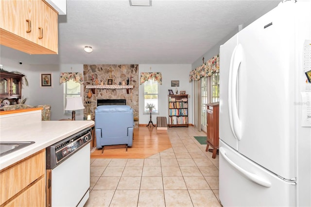 kitchen featuring white appliances, a textured ceiling, sink, light tile patterned floors, and a stone fireplace