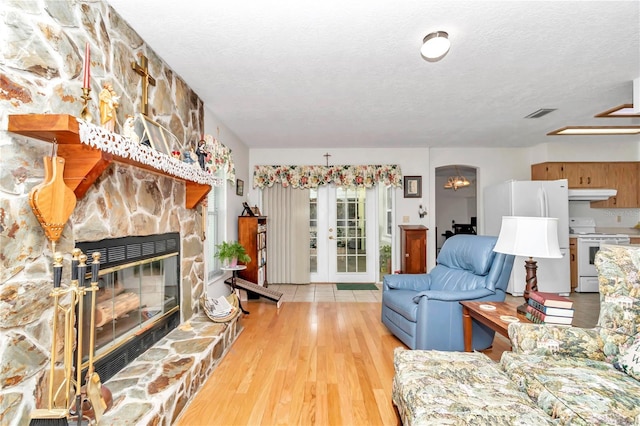 living room featuring a stone fireplace, light wood-type flooring, a textured ceiling, and a chandelier