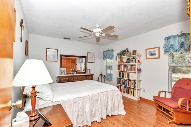 bedroom with multiple windows, ceiling fan, hardwood / wood-style floors, and a textured ceiling