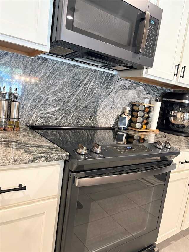 kitchen with stone counters, white cabinetry, appliances with stainless steel finishes, and backsplash