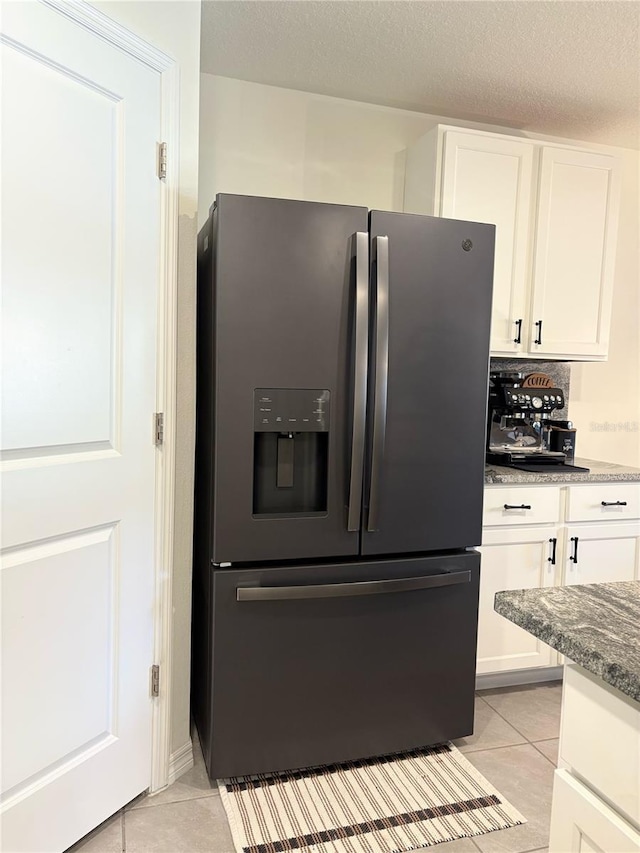 kitchen with stainless steel refrigerator with ice dispenser, light tile patterned floors, white cabinets, and dark stone counters